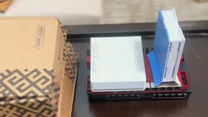 MikroTik routers stacked on a table beside an RB951-series retail box, the core hardware in a hotspot business budget